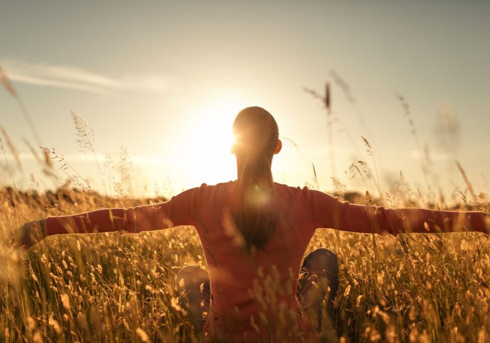 Person meditating in field at sunrise